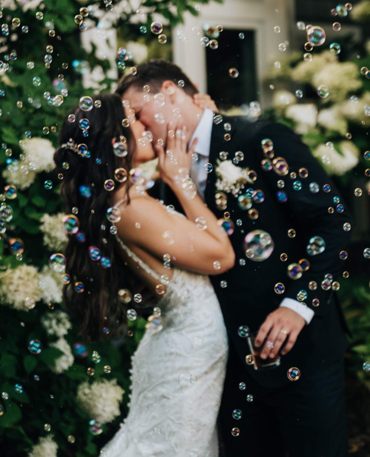 A bride and groom kissing in a cloud of bubbles in front of white hydrangeas