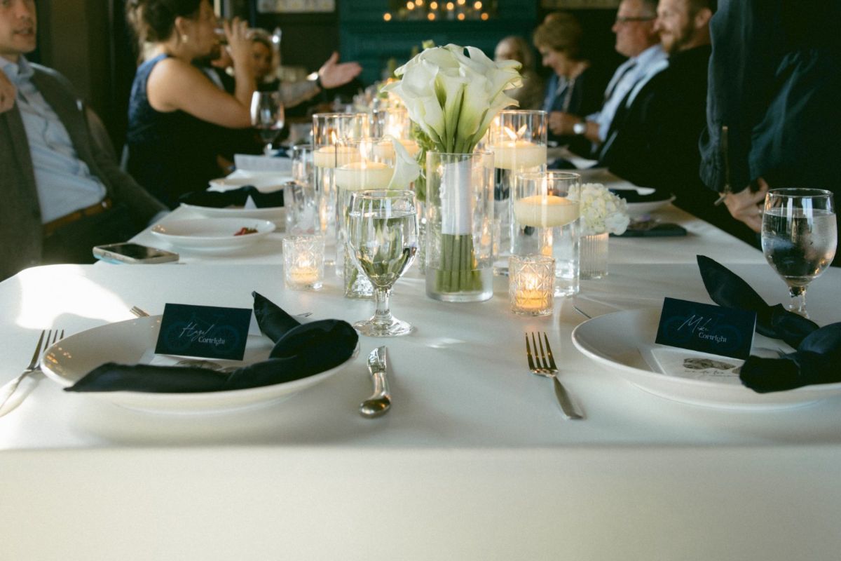 A candlelit reception table set with white calla lilies, floating candles, and navy napkins with place cards